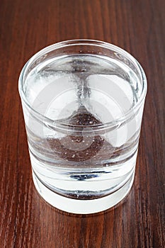 Glass of transparent purified water with ice on wooden table