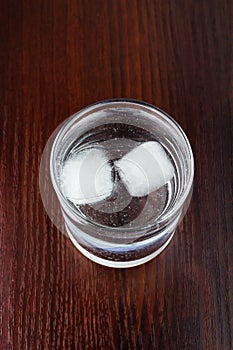 Glass of transparent purified water with ice on wooden table, top view