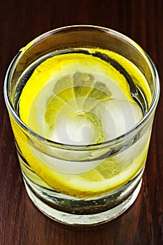 Glass of transparent purified water with slice of lemon and ice, on wooden table
