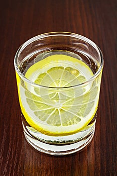 Glass of transparent purified water with slice of lemon, on wooden table