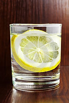 Glass of transparent purified water with slice of lemon, on wooden table