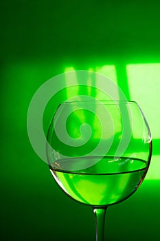 Glass of transparent white dry wine on green translucent background with window reflexion hard shadows. Conceptual creative