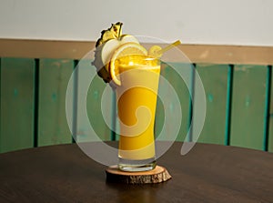 A glass of Tropical Twist juice shake of orange, apple, pineapple, mixed cocktail soda with raw fruits slice , lime and straw
