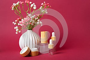 Glass tubes for creams next to a white vase with flowers on a background of magenta color