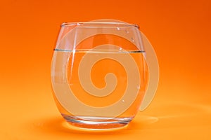 Glass tumbler with purified water on orange gradient background