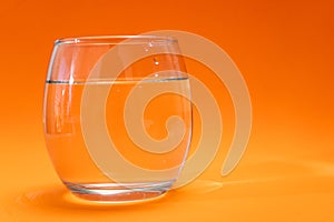 Glass tumbler with purified water on orange gradient background