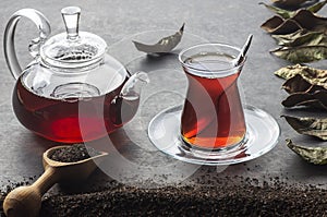 Glass Turkish brewed black tea and glass teapot with dry black tea and dried tea leaves on black rustic table