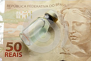 Glass vaccine bottle with liquid over a brazilian 50 Reais bank note from close