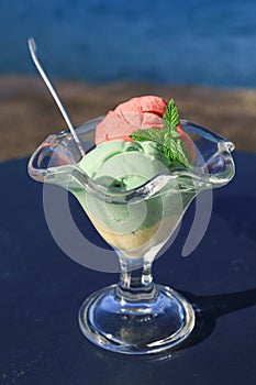 A glass of vanilla strawberry pistachio ice cream on the table by the sea.