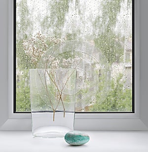 A glass vase on the background of a window with raindrops on the glass