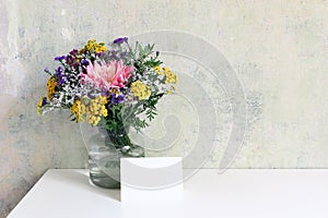 Glass vase with beautiful colorful bouquet of dahlia, tansies and aster flowers. Grunge old wall background. Feminine