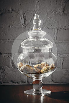 Glass vase with cookies and cover, on desk near grey wall