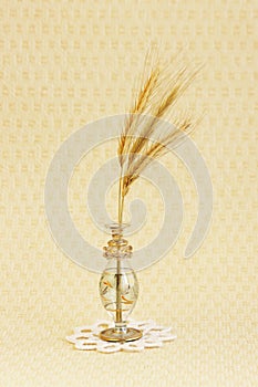 glass vase with a few ripe spikelets of rye Secale cereale on a white round knitted napkin on a beige background.