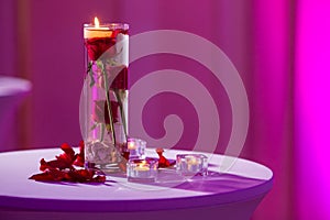 Glass vase with red roses water and light candles