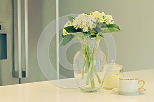 Glass vase of white flowers and teacup in a kitchen with blurred