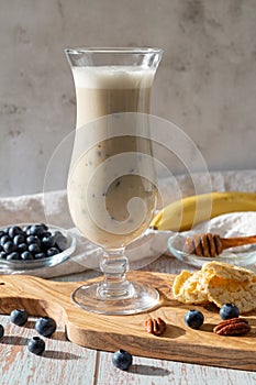 Glass of vegan cocktail or smoothy made from oat milk with bananas, blueberries and honey on an olive wooden board