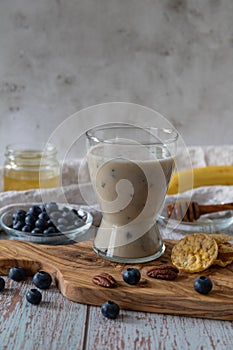 Glass of vegan cocktail or smoothy made from oat milk with bananas, blueberries and honey on an olive wooden board