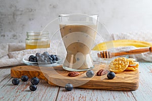 Glass of vegan cocktail or smoothy made from oat milk with bananas, blueberries and honey on an olive wooden board