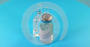 Glass vial filled with liquid vaccine and ampule rotate on blue background. Pharmaceutical industry. Viral infection treatment.