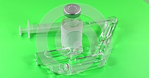 Glass vial filled with liquid vaccine and syringe rotate on green background. Pharmaceutical industry. Viral infection treatment.