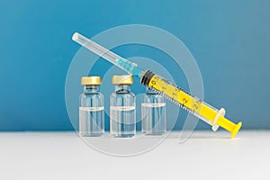 Glass vials with liquid and empty syringe on blue background. Coronavirus vaccine. nCov-2019 disease. Illness prevention.