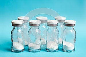 Glass vials of medicine in powder form lined up in a row on blue background