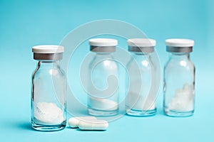 Glass vials with medicine in powder form and two white capsules on a blue background