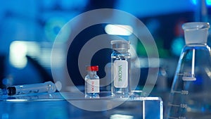 Glass vials with a vaccine and a syringe on a blurred laboratory background in blue light. Bottles with transparent