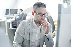 Through glass view of handsome worried man in business wear working on computer in bright office.