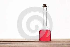 Glass vintage bottle with a brown cork and red liquid on a wooden table with white background.