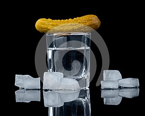 Glass vodka, pickled cucumber and ice cubes isolated on black.