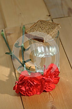 Glass of vodka and red carnations on a wooden table