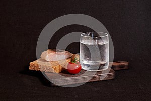 A glass of vodka, a sandwich with rye bread, herring and a cherry tomato