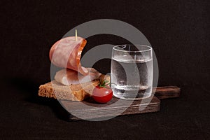 A glass of vodka, a sandwich with rye bread, herring and ham and a cherry