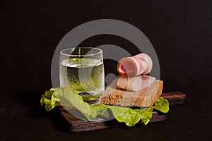 A glass of vodka, a sandwich with rye bread, herring and ham and lettuce