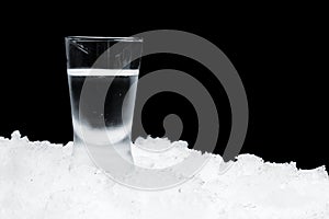 Glass of vodka standing on ice on black background