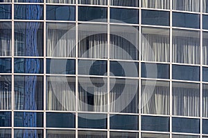Glass wall of modern building with other buildings reflection. Windows are closed with curtains