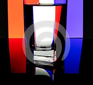 Glass of water against a three-color background. Water in refracting light.