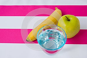 A glass of water, an apple and a banana on a tablecloth
