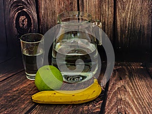 Glass of water,banana and green apple on wooden background