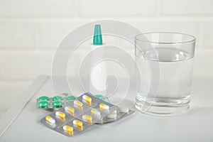 Glass of water and blister packages of pills on light table background