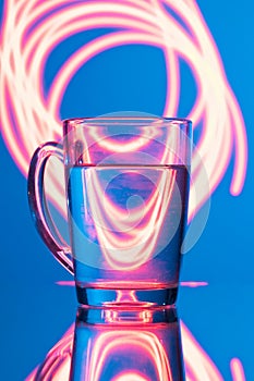 Glass of water on a blue background with a yellow abstraction, glare of light