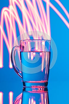 Glass of water on a blue background with a yellow abstraction, glare of light