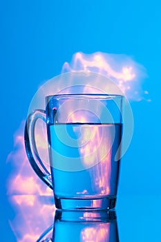 Glass of water on a blue background with a yellow abstraction, glare of light