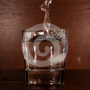 A clear stream of water pours into a glass on a braun background photo