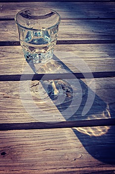 Glass of water casting shadow on wooden table - vignette photo