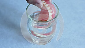 A glass of water containing removable dentures. The man`s hand takes the false teeth from the glass. Dental prosthetics theme. den