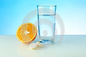 A glass of water, effervescent pill and orange on blue background with copy space. vitamin C concept.