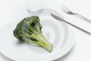 Glass of water, fork, knife and broccoli on the plate