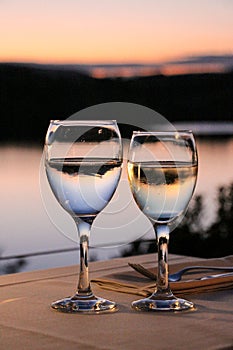 Glass of water and glass of wine on a table in a restaurant with a sunset view at the lake Marathon, Greece.